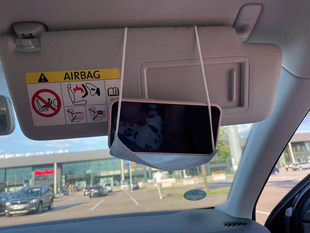 Blick aus dem Auto Handy hängt am Sonnenschutz in einer medizinischen Maske